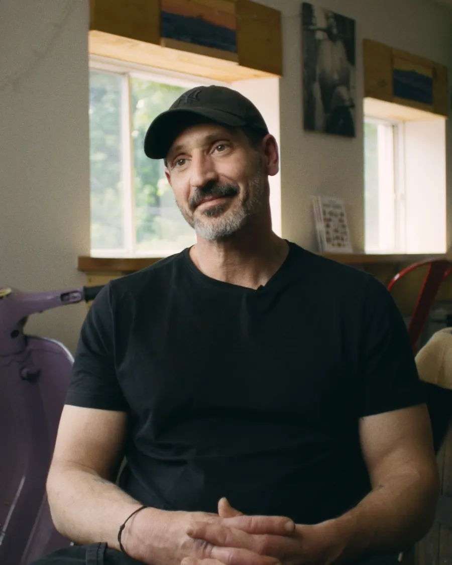 A man sits in a cafe and looks directly at a camera.